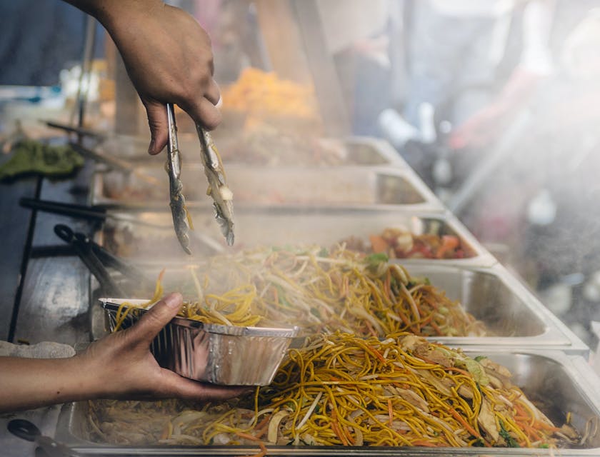 Una persona che lavora in uno stand gastronomico mentre mette del cibo in un contenitore di alluminio.