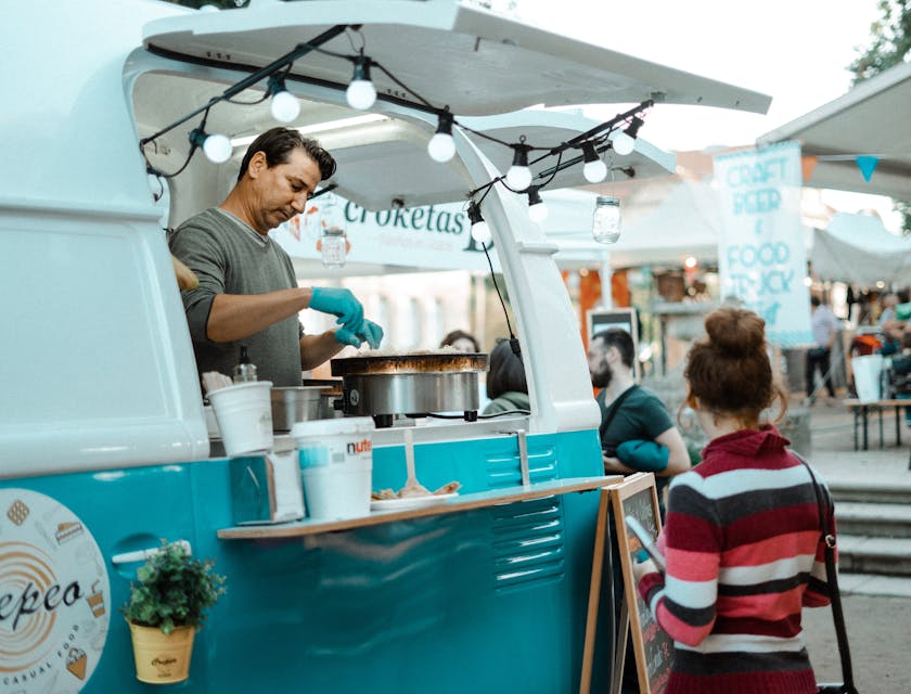 A man serving a woman who is standing outside a food truck.