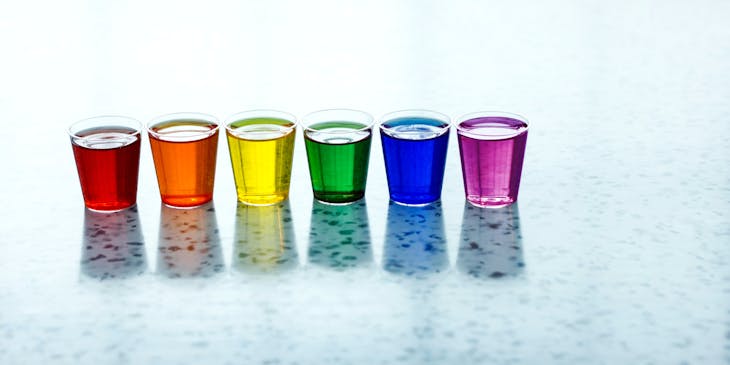 Shot glasses on a surface with multi-colored liquids at a gay bar.