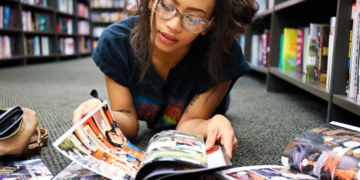 Une femme geek à lunettes lisant une bande dessinée sur le sol d'une librairie.