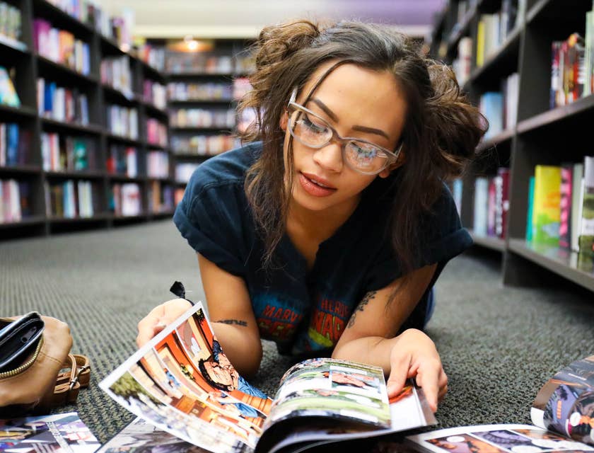 Une femme geek à lunettes lisant une bande dessinée sur le sol d'une librairie.