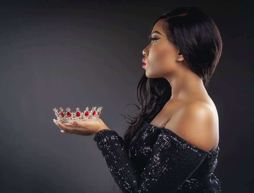 Una donna dallo stile glamour vestita di nero che tiene in mano una corona con pietre preziose rosse.