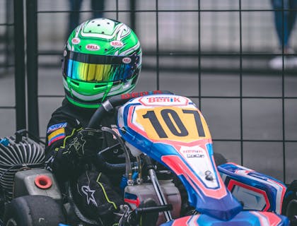 Ein Kind mit grünem Helm und der Startnummer 107 sitzt in einem blauen Go-Kart und wartet auf den Beginn einer Rennrunde.