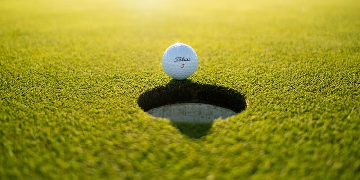 A golf ball in the sunlight resting on the green.