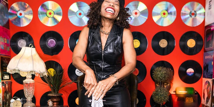 A groovy woman with a guitar standing in front of a wall of records.