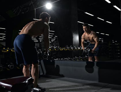 Un uomo che si allena con dei pesi davanti allo specchio in una palestra.