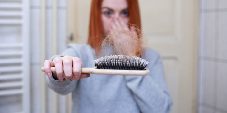 Woman holding out brush with loose hair on showing hair loss.
