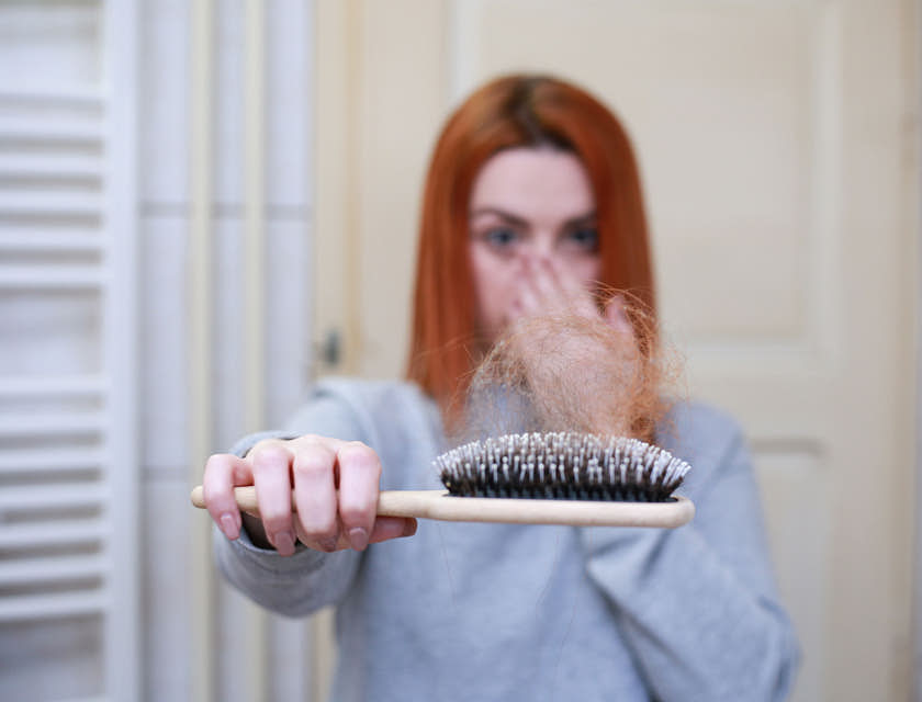 Mulher com perda de cabelo segurando uma escova cheia de fios de cabelo.