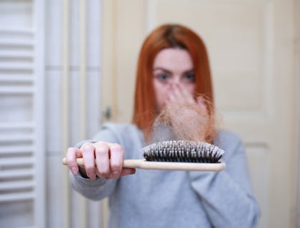 Woman holding out brush with loose hair on showing hair loss.