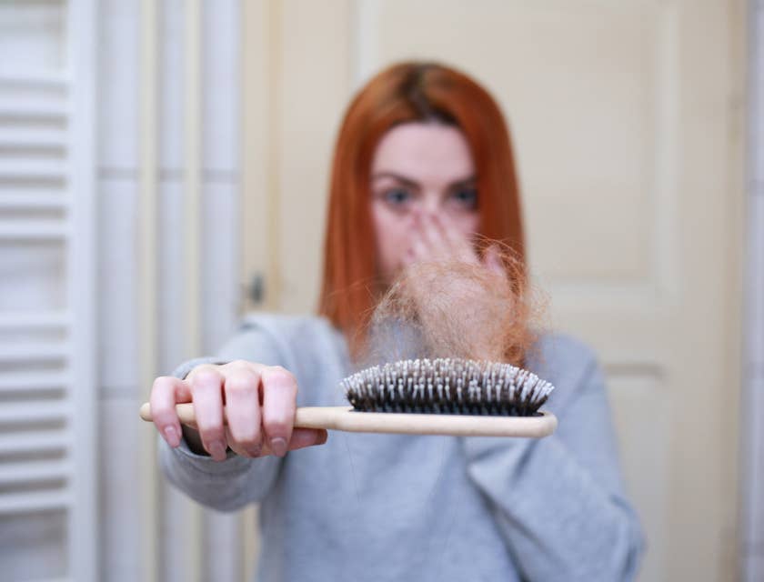 Una donna che tiene in mano una spazzola per mostrare i capelli che le sono caduti.