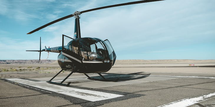 A black helicopter on a landing strip below a blue sky.