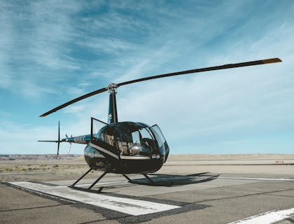 A black helicopter on a landing strip below a blue sky.