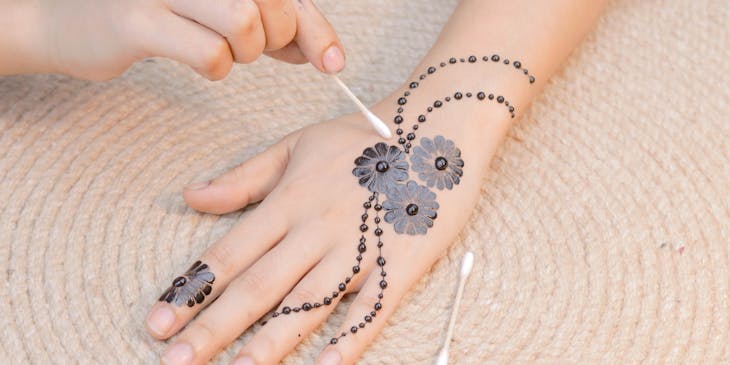 Cotton swab being used to apply a flower pattern in henna onto a hand.