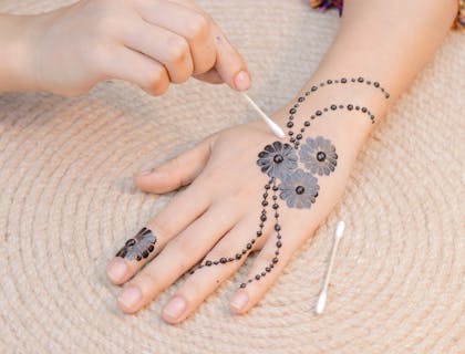 Cotton swab being used to apply a flower pattern in henna onto a hand.