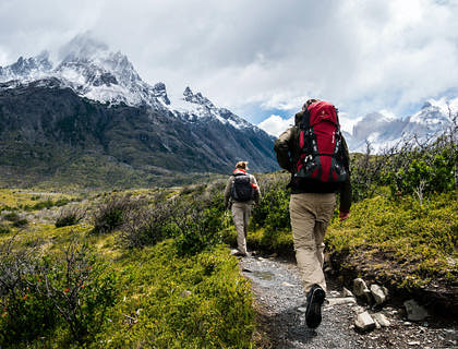 Two hikers walking a hiking trails towards a mountain covered in snow.