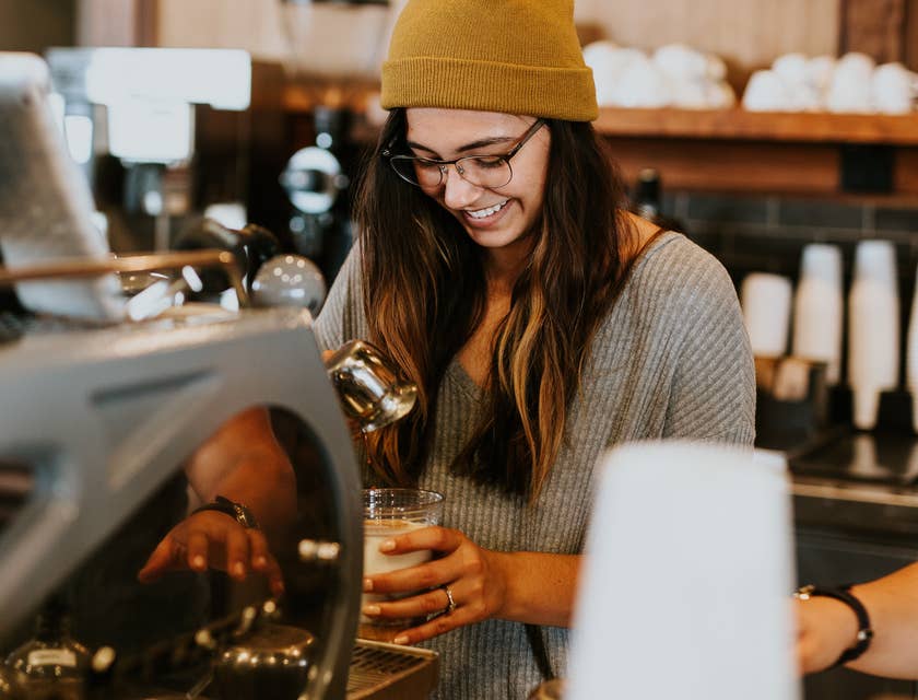 Mulher com gorro e óculos de estilo hipster fazendo café em uma cafeteria.