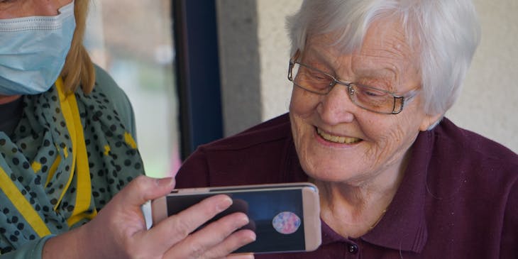 Nurse holding up a cellphone for an elderly woman to see the screen in a home.