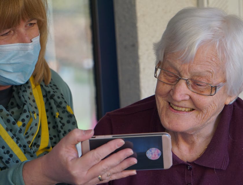 Nurse holding up a cellphone for an elderly woman to see the screen in a home.