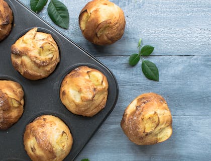 a freshly-baked apple muffin alongside a tray containing more muffins