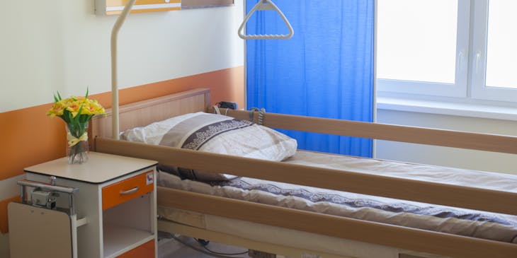 Bed with rails situated next to a blue screen in a naturally-lit hospice room.