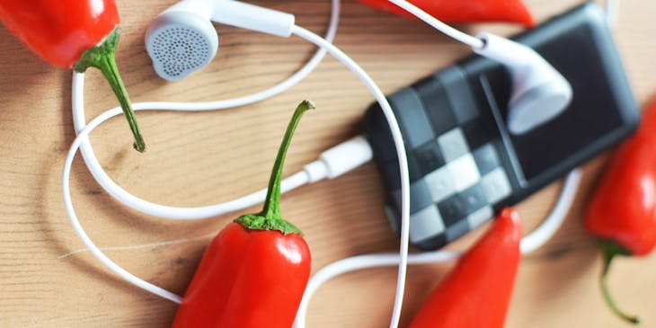 A music player with earphones and hot chilies on wooden surface.