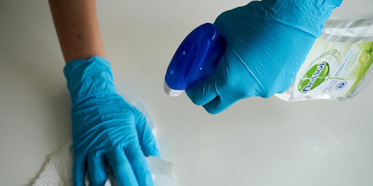 Person donning blue gloves while sanitizing a white surface using Dettol.