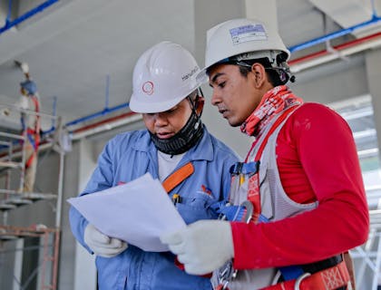 two people in hard hats and safety gear looking at papers