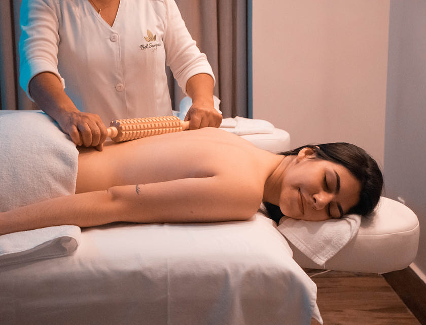 woman lying down on massage table getting massage with wooden roller