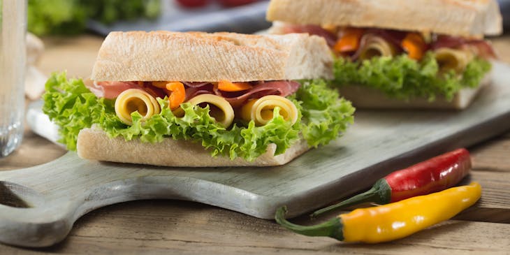 Sándwich con lechuga y queso servido encima de una tabla para picar en una tienda delicatessen.