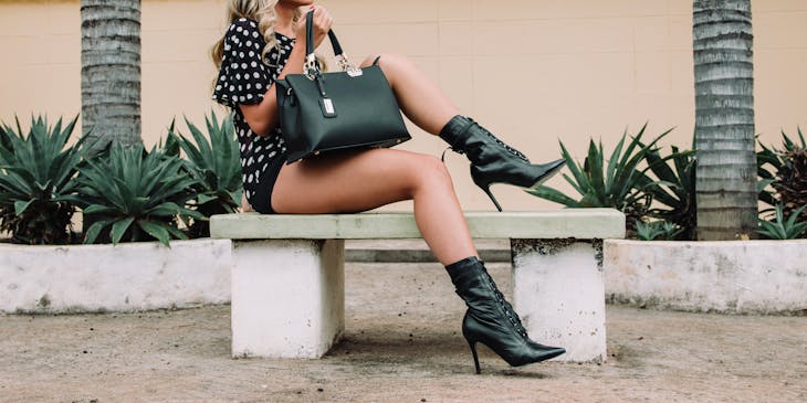 woman in fashionable clothing with sunglasses and large black leather purse sitting on bench
