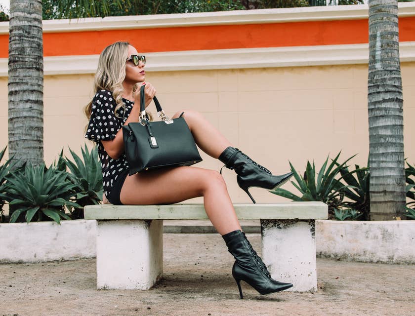 woman in fashionable clothing with sunglasses and large black leather purse sitting on bench