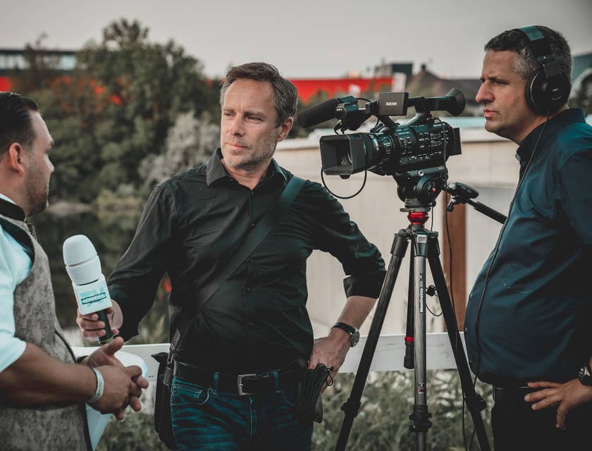 Un reportero con micrófono entrevistando a un hombre frente a la cámara de una agencia de medios.