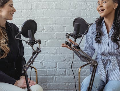 Two women talking in front of microphones and recording a podcast.