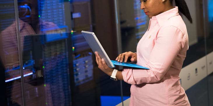 Mujer con una computadora portátil parada frente a los servidores en una empresa de tecnología.