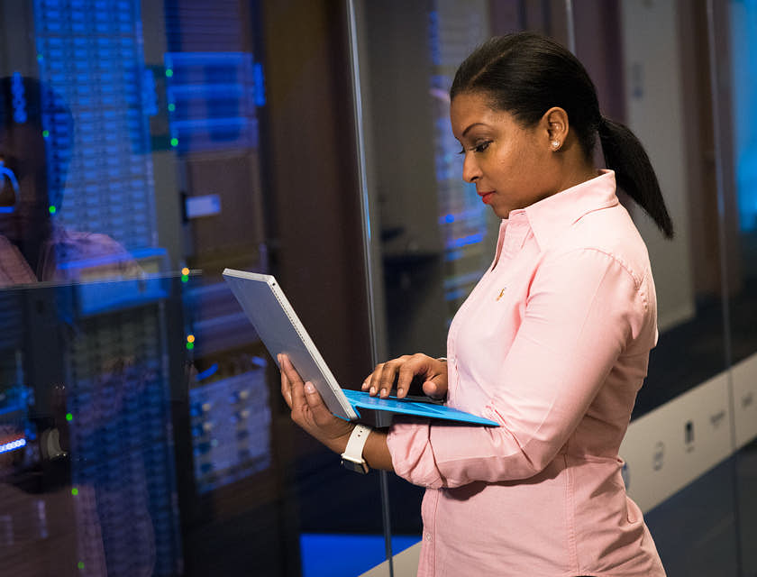 Mujer con una computadora portátil parada frente a los servidores en una empresa de tecnología.