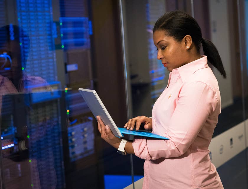 Mujer con una computadora portátil parada frente a los servidores en una empresa de tecnología.