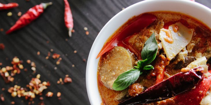 bowl of red curry soup with hot pepper and basil leaf