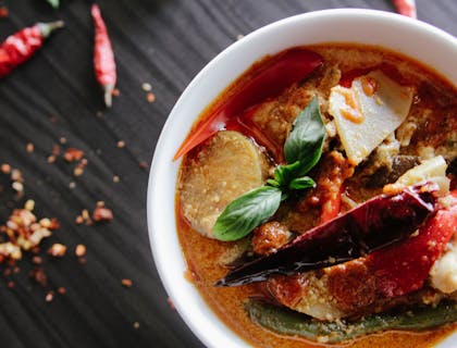 bowl of red curry soup with hot pepper and basil leaf