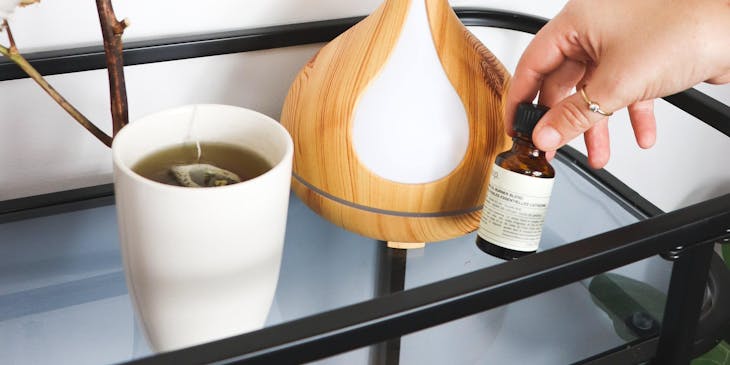 A person holding a bottle of essential oil next to an aromatic diffuser.