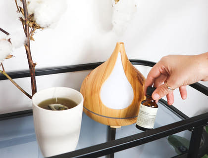 Una persona sosteniendo una botella de aceite esencial junto a un difusor aromático.