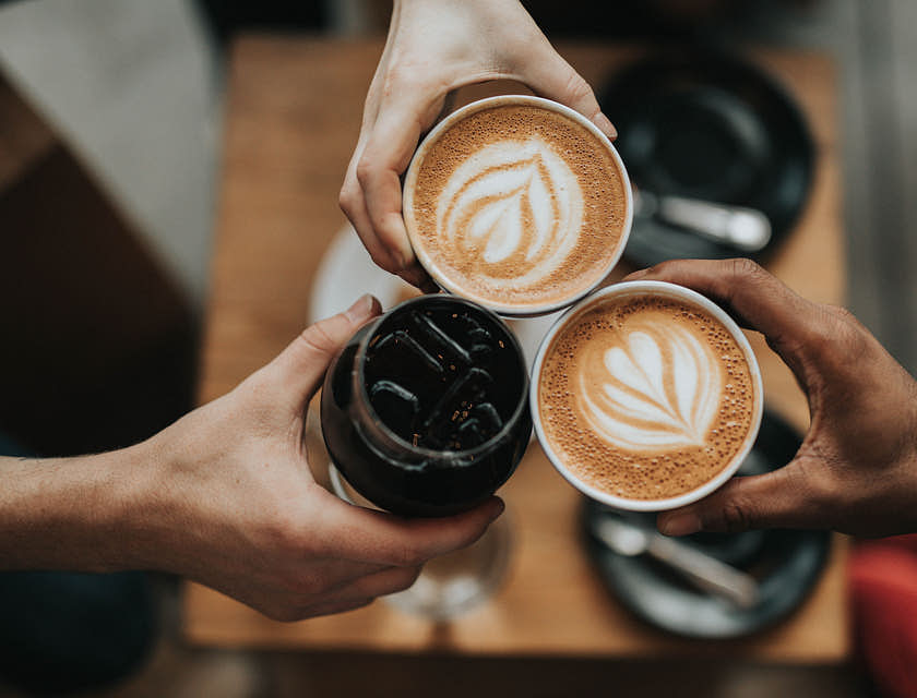 Tres manos sosteniendo cafés capuchinos en un café.