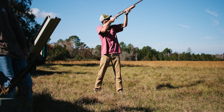 Man taking aim with hunting rifle on open field.