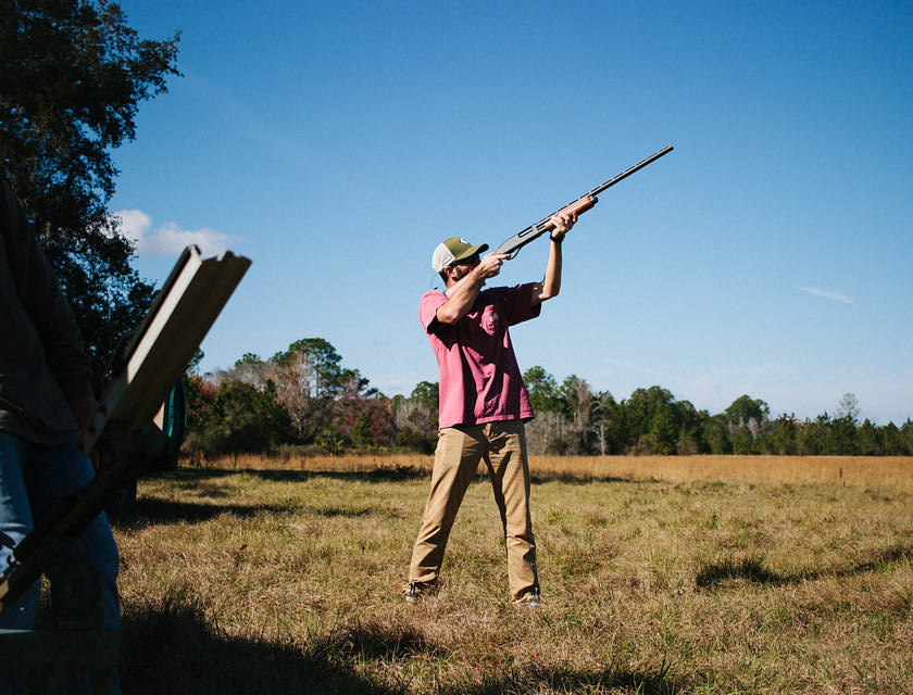 Homme avec un chapeau qui vise une proie avec un fusil de chasse.