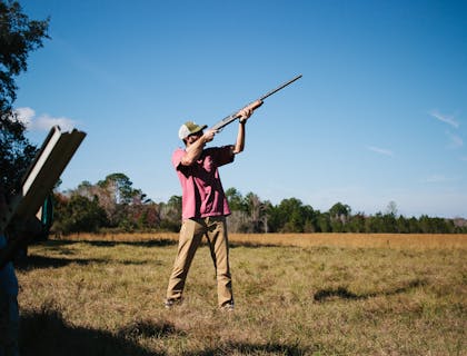Hombre apuntando con su rifle en un campo de negocio de caza.