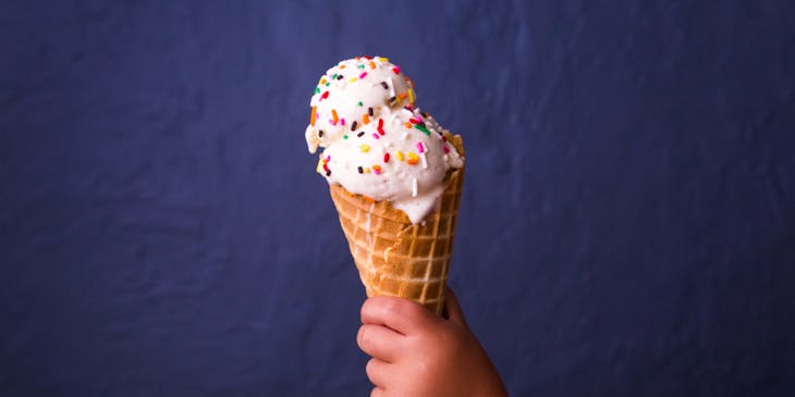 Toddler holding an ice cream cone with two scoops of ice cream and sprinkles.