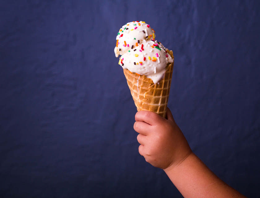 Un bambino con in mano un cono gelato ricoperto di praline colorate.