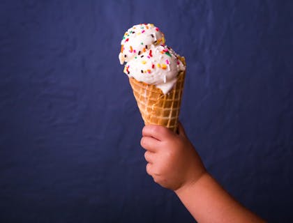 Toddler holding an ice cream cone with two scoops of ice cream and sprinkles.