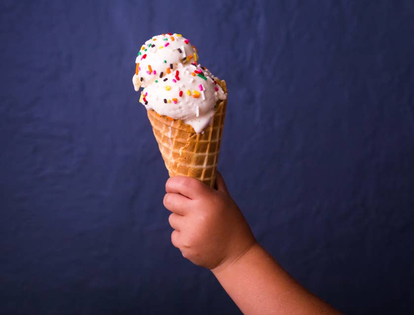 Un jeune enfant tenant un cornet de glace avec deux boules de glace et des vermicelles au chocolat de toutes les couleurs.