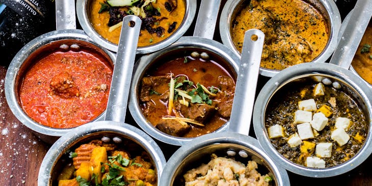 Mini silver pots filled with different curries in an Indian restaurant.