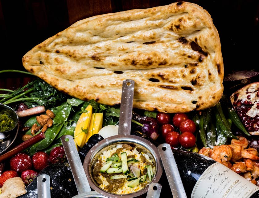 Ein Tisch mit kleinen, silbernen Töpfen, die mit verschiedenen Curries gefüllt sind, Naan-Brot und anderen Spezialitäten in einem indischen Restaurant.